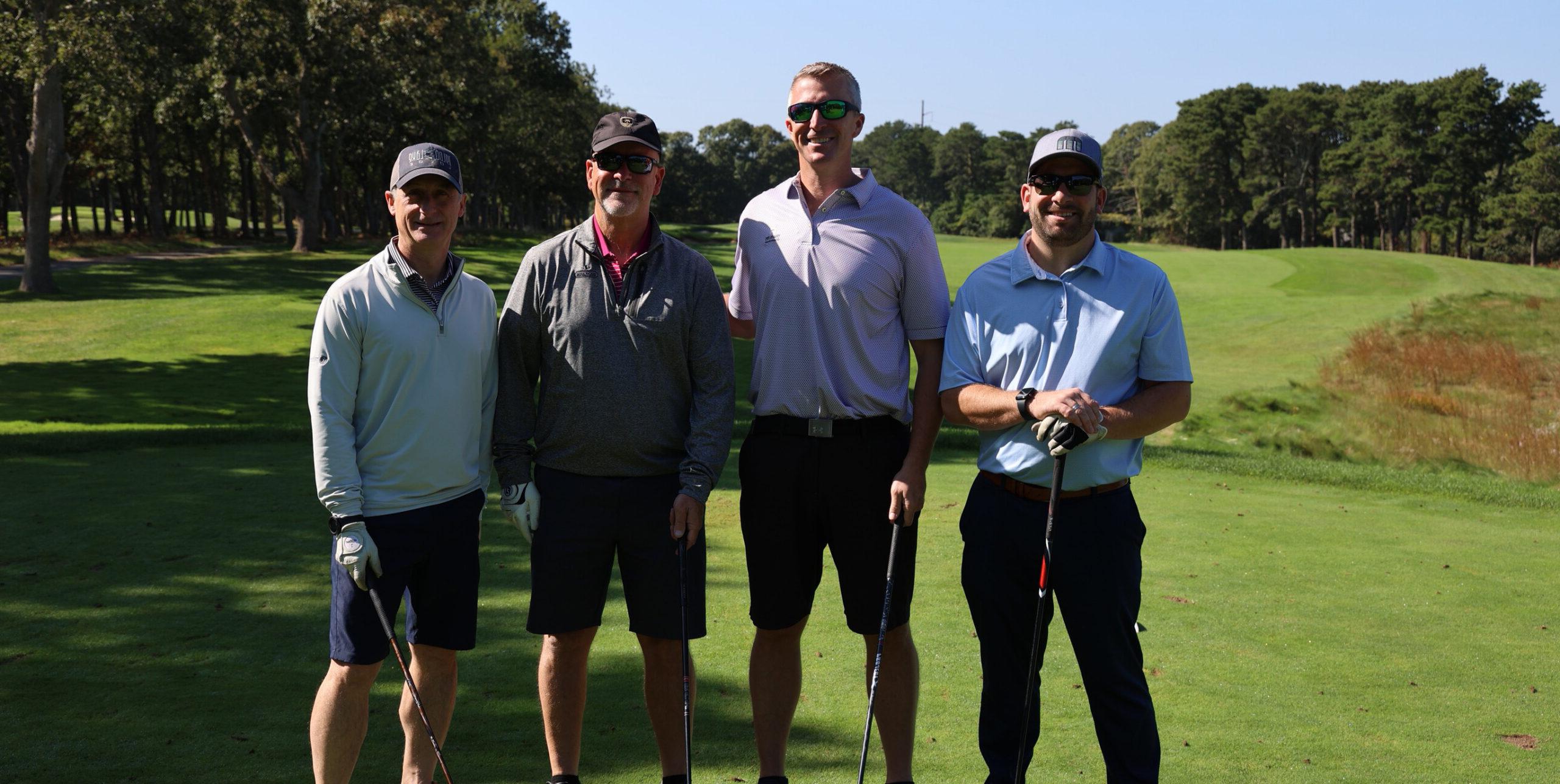 4 people st和ing with golf clubs on a golf course.